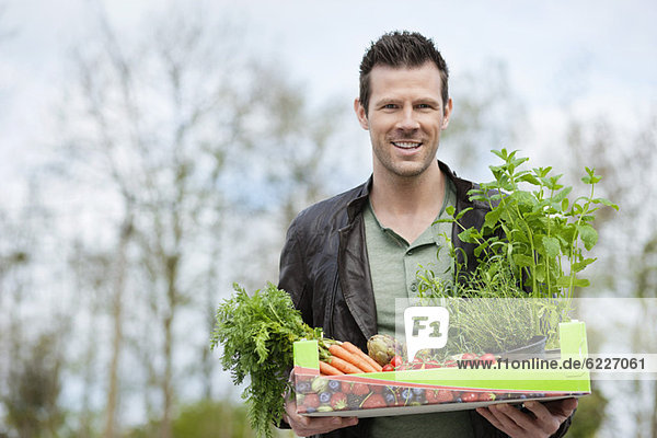 Mann hält ein Tablett mit rohem Gemüse.