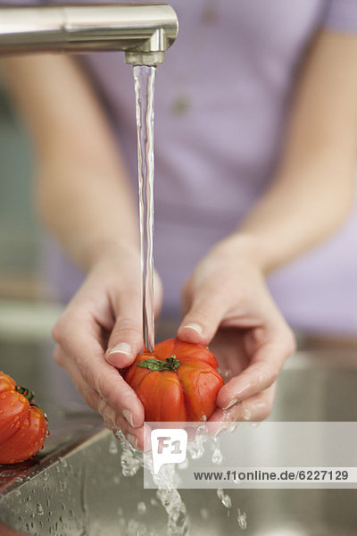 Frau wäscht Tomaten in der Küche
