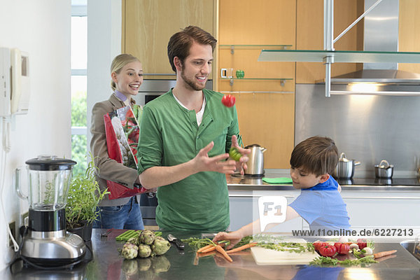 Eltern  die ihren Sohn beim Gemüseschneiden in der Küche anschauen