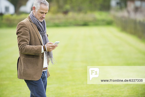 Man Textnachrichten auf einem Mobiltelefon in einem Park