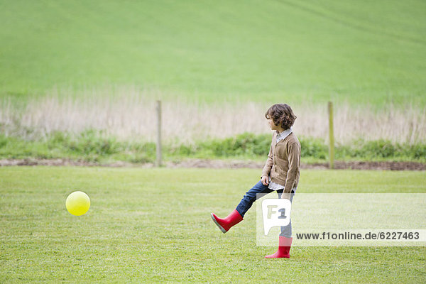Junge spielt mit einem Ball auf einem Feld