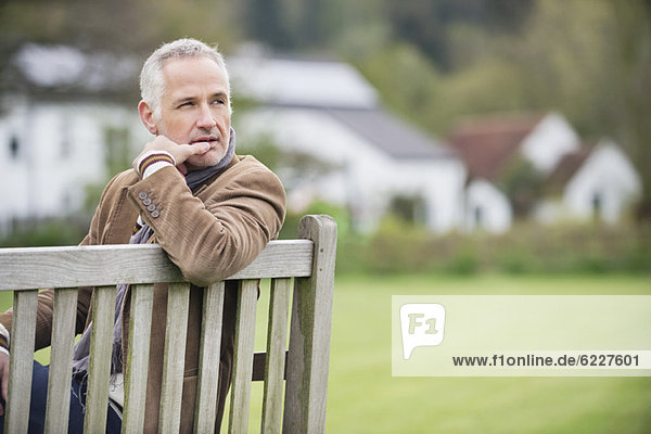 Mann sitzt auf einer Bank und denkt in einem Park