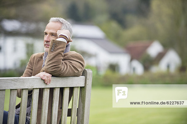 Mann sitzt auf einer Bank und denkt in einem Park