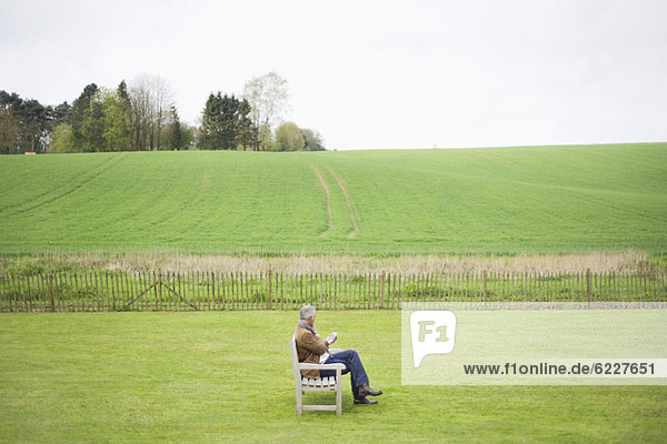 Mann  der auf der Bank sitzt und ein Handy auf dem Feld benutzt.