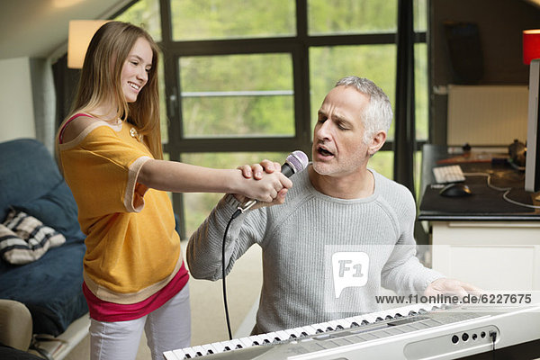 Mann singt und spielt mit seiner Tochter zu Hause Klavier.