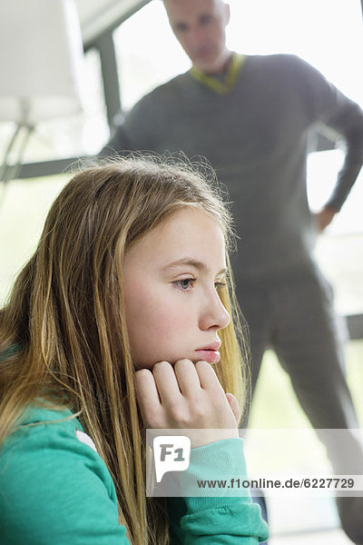 Ein Mädchen sieht verärgert aus  wenn ihr Vater neben ihr steht.