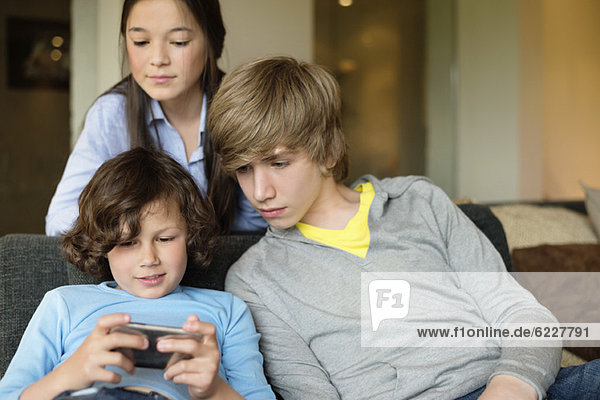 Boy using a cellphone with his brother and sister at home
