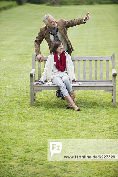 Mann sitzt mit seiner Tochter auf einer Bank und zeigt in einen Park.