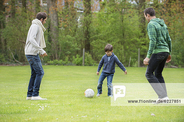 Boy playing soccer with two men in a park