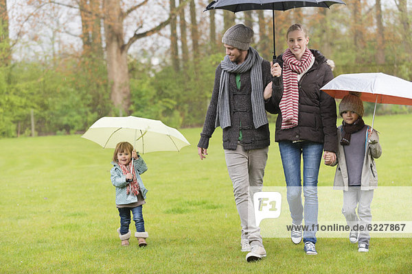 Family walking with umbrellas in a park
