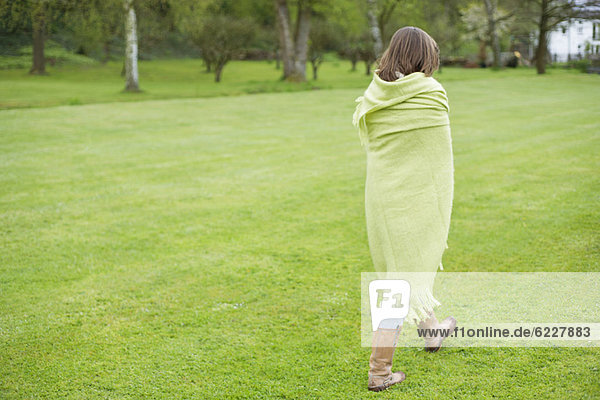 Mädchen in eine Decke gehüllt und auf einem Feld gehend