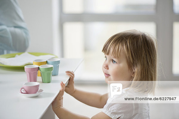 Süßes Mädchen mit Spielzeug Teeservice neben einem Esstisch
