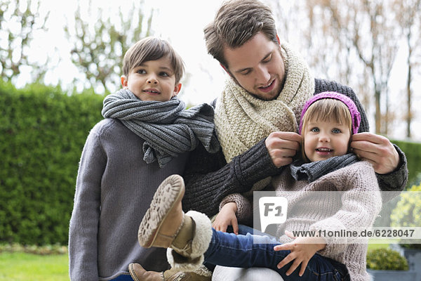 Man with his son and daughter in warm clothing in a park