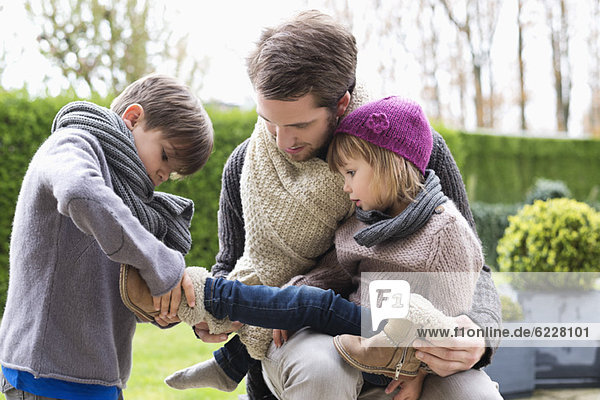 Boy putting shoe on his sister sitting in her father's lap