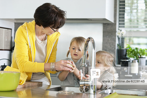 Ältere Frau mit ihren Enkelinnen beim Waschen in der Küche