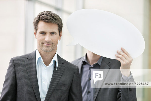 Portrait of a businesswoman smiling with her colleague holding speech bubble behind her