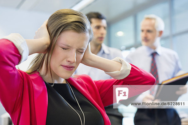 Female executive looking frustrated in an office with her colleagues discussing in the background