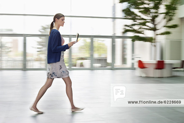 Geschäftsfrau  die Dokumente hält und in einer Bürolobby spazieren geht.