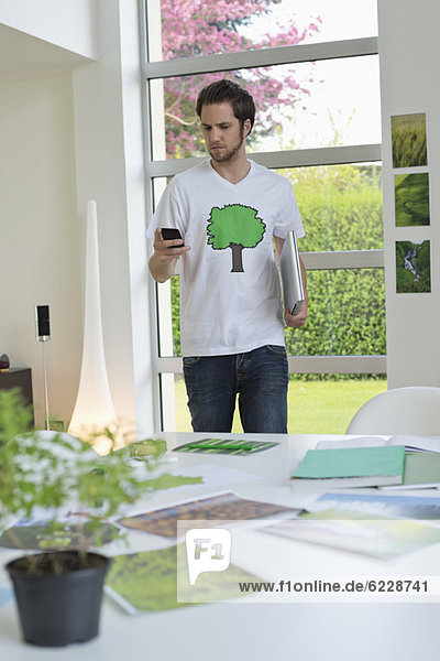 Mann  der ein Mobiltelefon mit umweltbezogenen Plakaten vor sich auf einem Tisch benutzt.