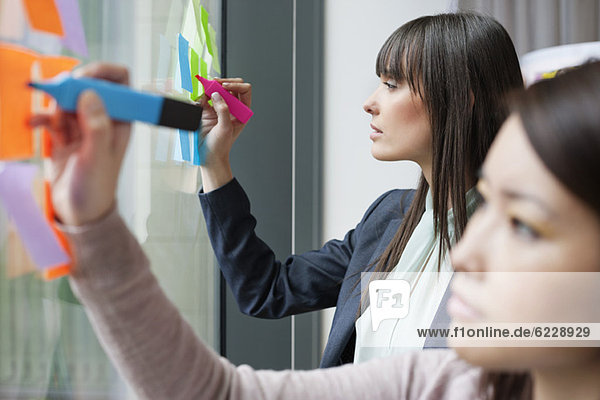 Businesswomen writing on adhesive notes in an office