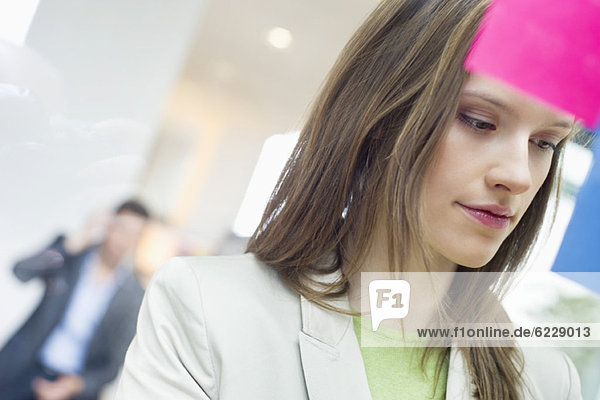 Geschäftsfrau klebt Notizzettel auf Glas im Büro