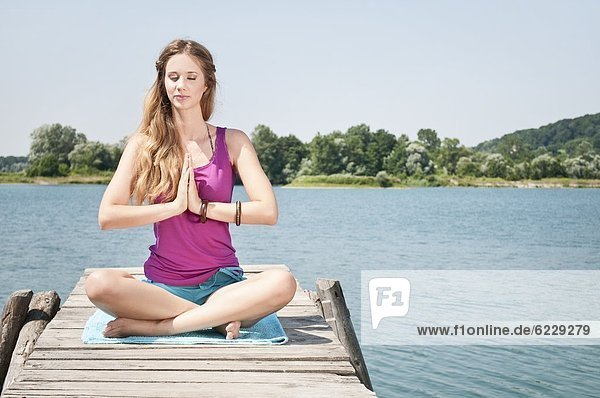 Blonde junge Frau macht Yoga an einem See