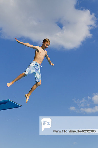 Boy jumping from the three-metre diving board at an outdoor swimming pool