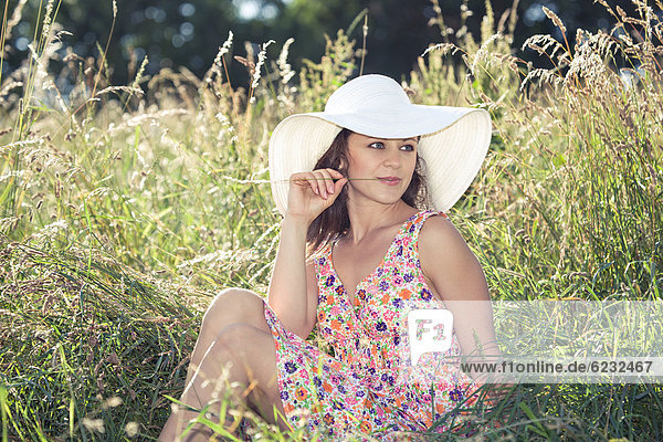Junge Frau mit Hut und Sommerkleid in hohem Gras