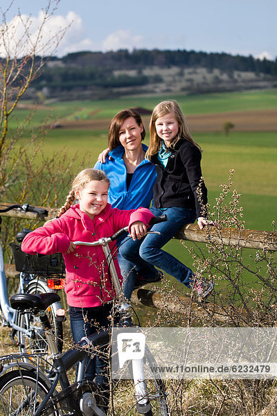 Mutter und zwei Töchter mit Fahrrädern in ländlicher Umgebung