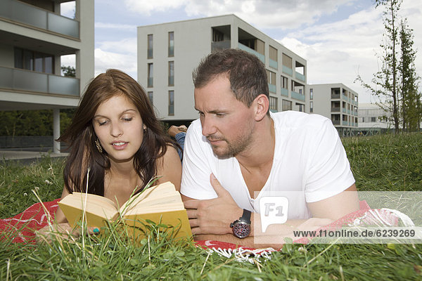 Young couple lying in meadow reading book