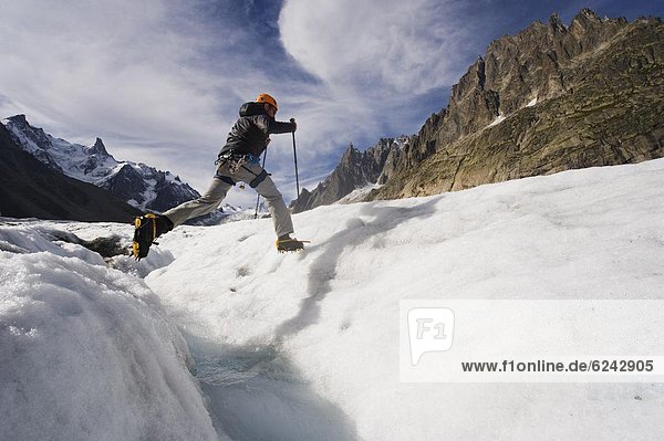 Climber jumping across a crevase stream on Mer de Glace glacier  Mont Blanc range  Chamonix  French Alps  France  Europe