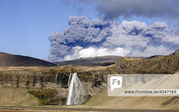 Distant view of the Seljalandsfoss waterfall with the ash plume of the Eyjafjallajokull eruption in the distance near Hella southern Iceland Iceland Polar Regions