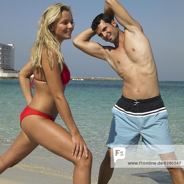 Couple on beach doing stretching exercises