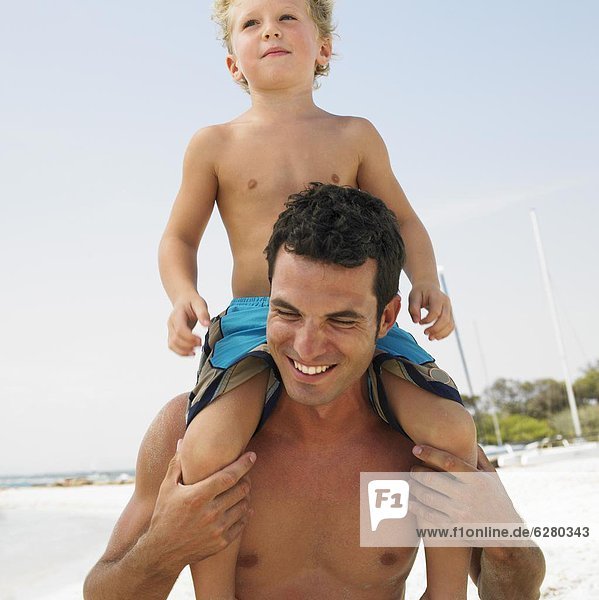 Son (6-8) sitting on father's shoulders on beach