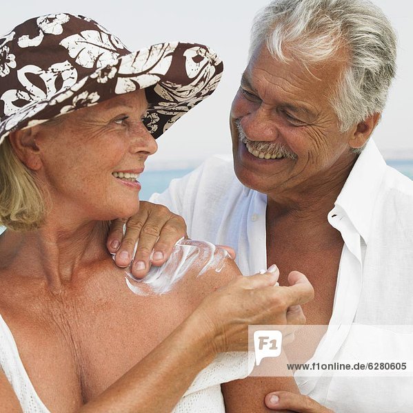 Senior couple on beach  man applying suncream to woman