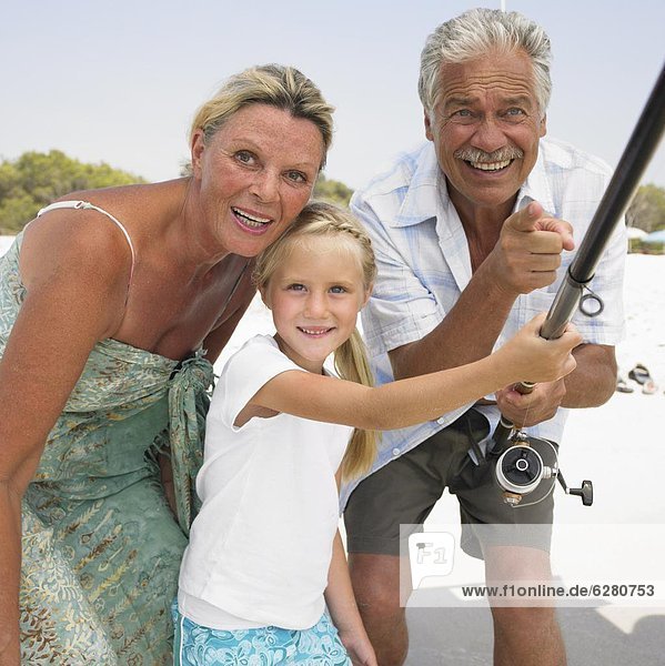 Grandparents and grandaughter (6-8) on beach holding fishing rod