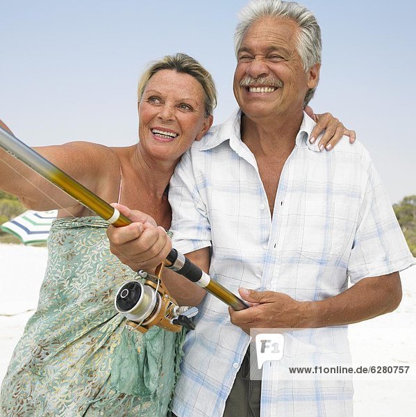 Senior couple on beach  man holding fishing rod