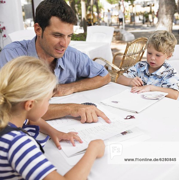 Father and two children (6-8) sitting at an outdoor cafe