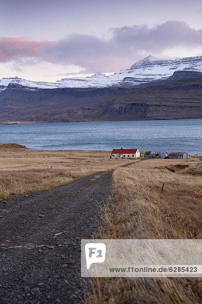 Red-roofed house and snow-capped mountains in Reydarfjordur fjord  East Fjords  Iceland  Polar Regions