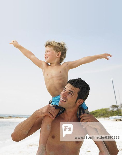Son (6-8) sitting on father's shoulders on beach