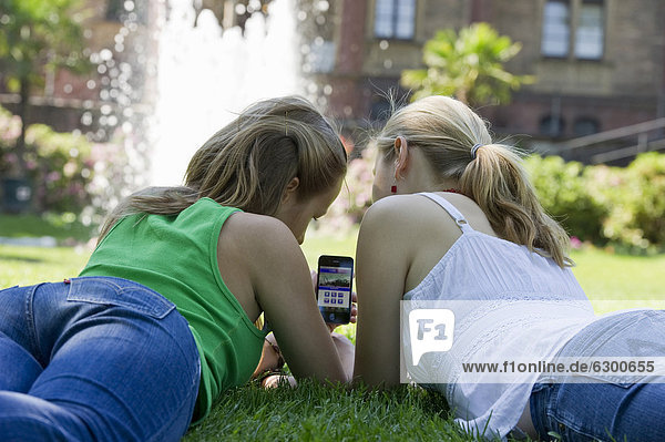 Two young women with a smartphone  lying on a meadow