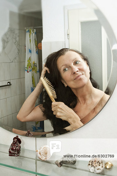Frau bürstet ihre Haare vor dem Spiegel im Badezimmer