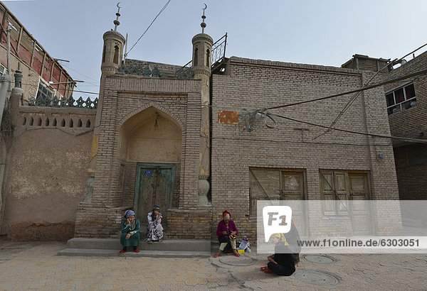 Muslim women  Uighurs with colourful headscarves sitting in front of a mosque  mud-brick houses  Uighur historic centre of Kashgar  Silk Road  Xinjiang  China  Asia