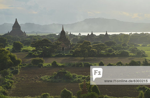 Smoke rising  fog in the evening light between fields  temples and pagodas  Ananda Temple and Thatbyinnyu Temple  Bagan  Myanmar  Burma  Southeast Asia  Asia