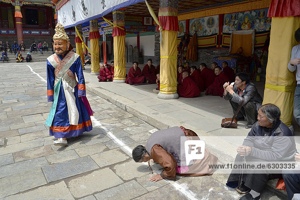 Tibetan Buddhism  woman kneeling in prayer to the religious masked Cham dance  at the important Kumbum Monastery  Gelug or Gelug-pa yellow hat sect  Ta'er Monastery  Huangzhong  Xinning  Qinghai  formerly Amdo  Tibet  China  Asia