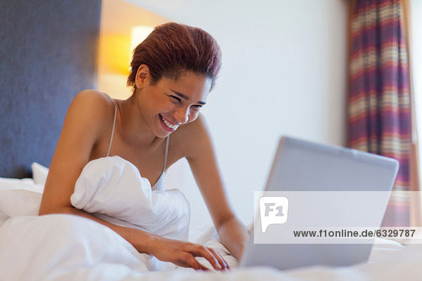 Happy young woman using laptop in bed