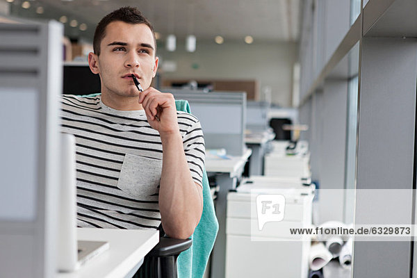Man chewing pen at desk