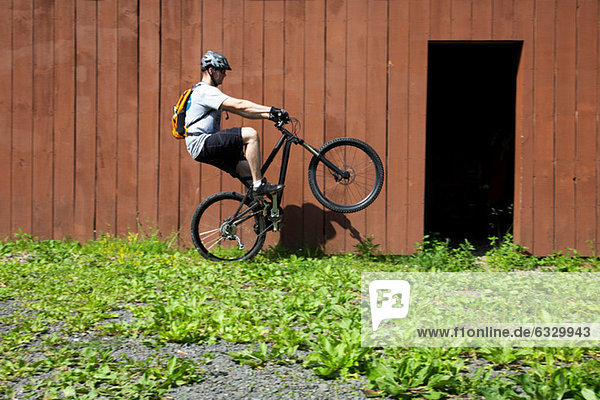 Mountain biker riding on one wheel outside barn