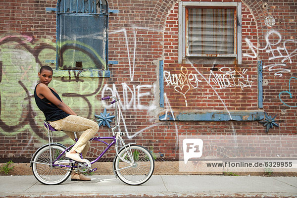 Portrait of a young woman on bicycle by wall covered in graffiti