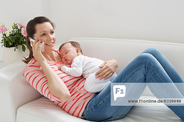 Mutter auf dem Sofa mit Baby auf dem Handy